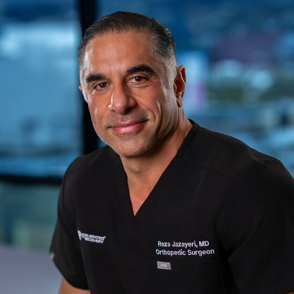 Professional headshot of Dr. Reza Jazayeri, MD, Orthopedic Surgeon, wearing black scrubs against a blurred blue city skyline background.