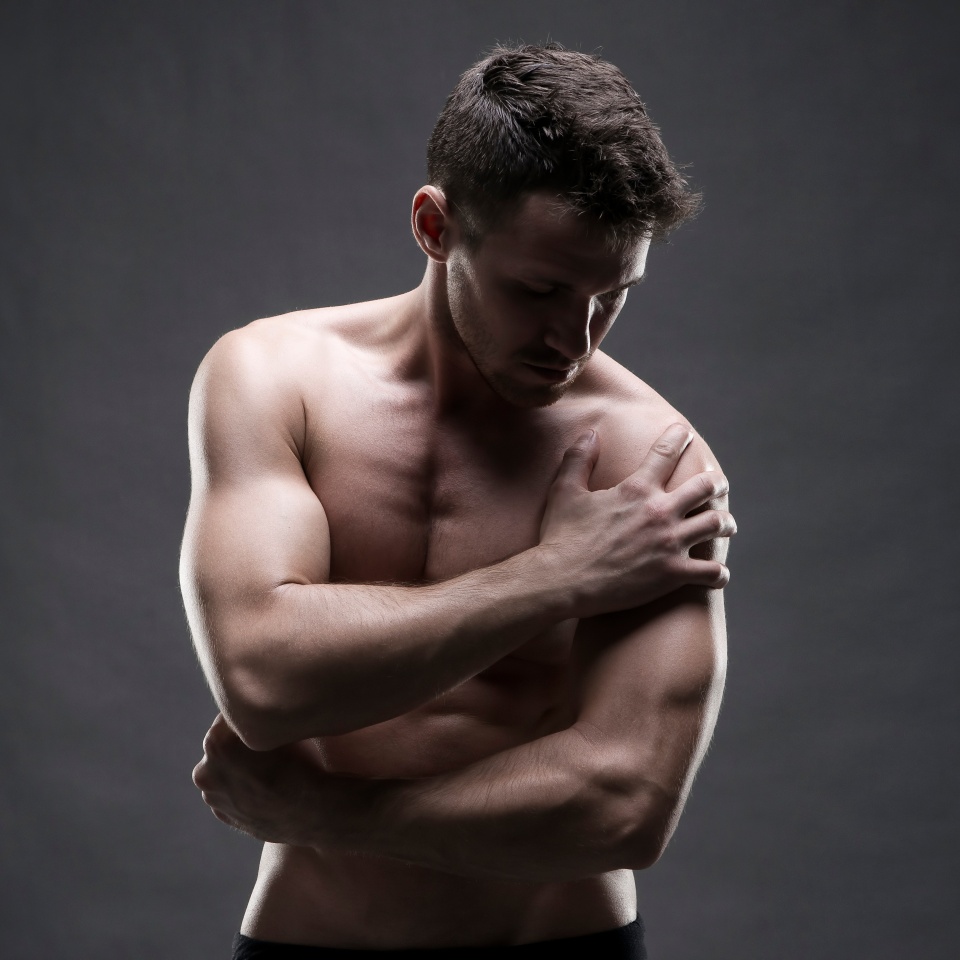Pain in the shoulder. Muscular male body. Handsome bodybuilder posing on gray background. Low key close up studio shot. Middle part of the body