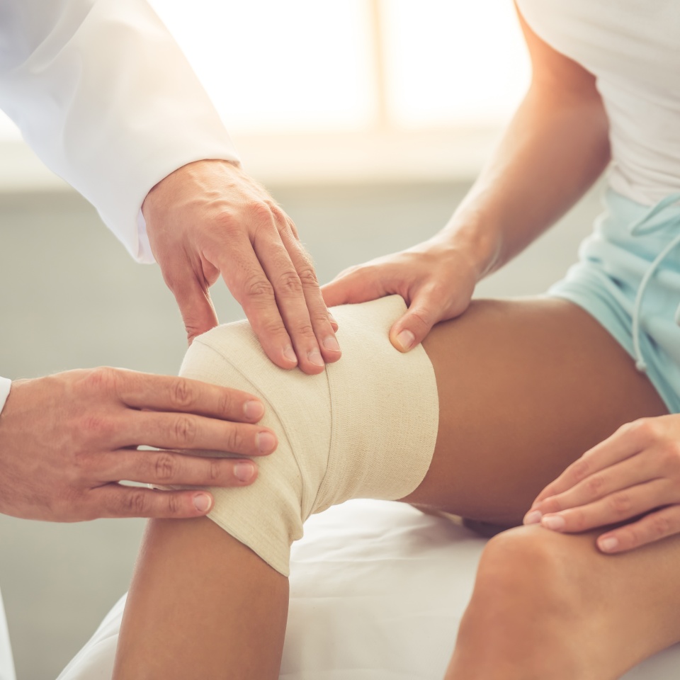 Cropped image of handsome doctor bandaging woman's injured knee while working in his office