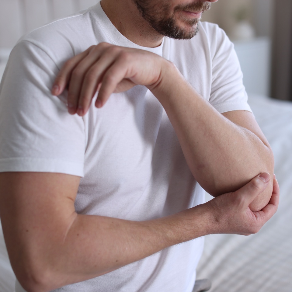 Man suffering from elbow pain on bed at home, closeup