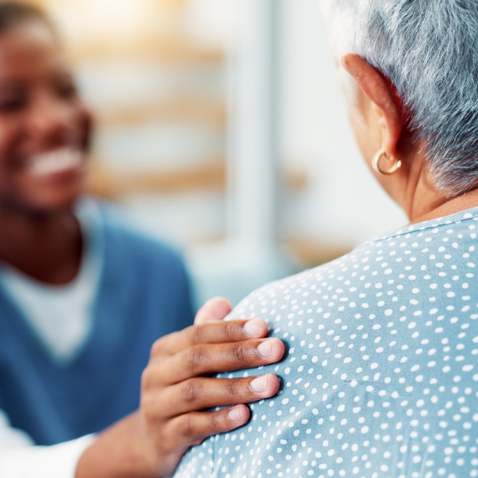 Senior woman, nurse and hand on shoulder for support, healthcare and medical wellness in home. Retirement, patient and comfort with caregiver in living room for help, kindness and empathy with trust.
