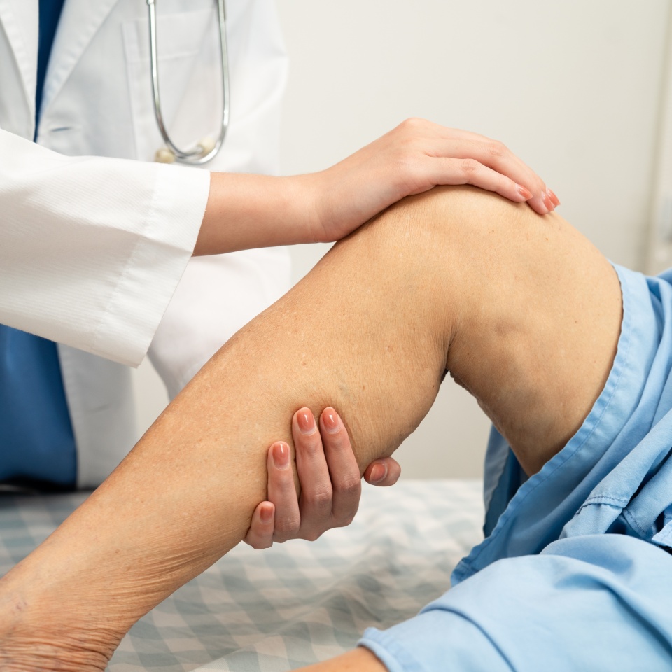 Doctor checking Asian elderly woman patient with scar knee replacement surgery in hospital.