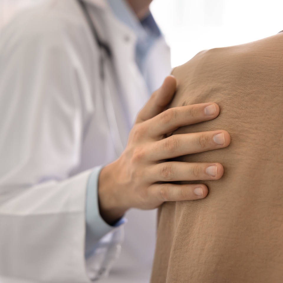 Close up male doctors hand gently resting on female patients shoulder, symbolizing empathy and psychological support during sensitive or difficult conversation about disease news or further operation