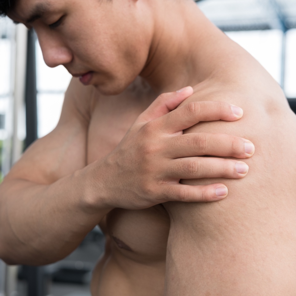 muscular male having pain on shoulder in gym. young man injure while workout in fitness center. asian bodybuilder feel hurt while exercise at health club. Sports injury, muscle intense.