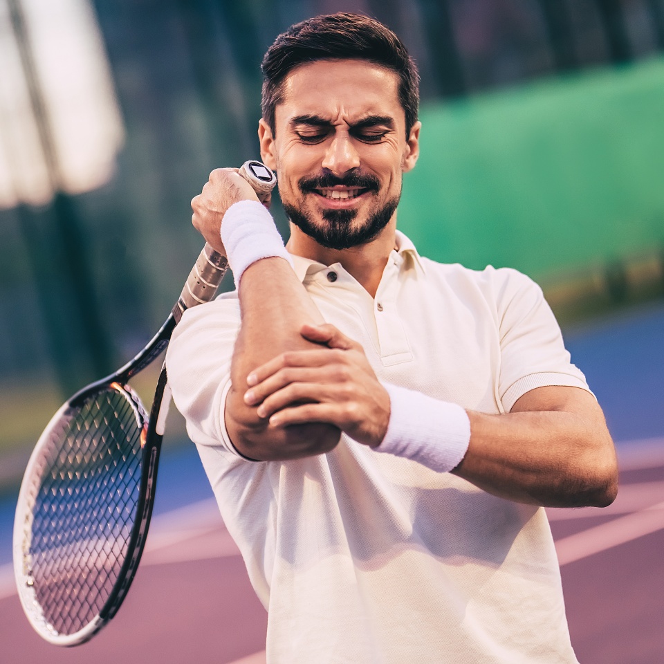 Handsome man on tennis court. Young tennis player. Pain in the elbow