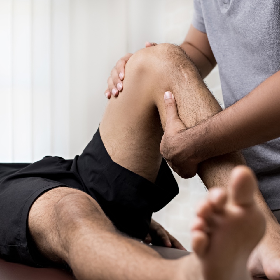 Therapist treating injured knee of athlete male patient in clinic - sport physical therapy concept