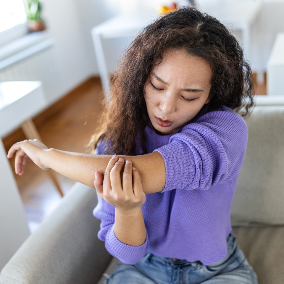 Elbow pain and injury. People with body-muscles problem, Healthcare And Medicine concept. Asian woman sitting on the sofa and holding painful elbow with hand. Joint inflammation and ache concept.