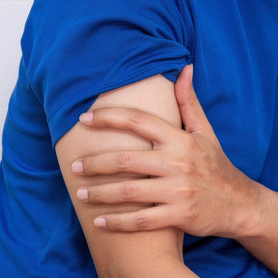 A person wearing a blue shirt is holding their upper arm with their other hand, suggesting possible pain or discomfort in the arm.