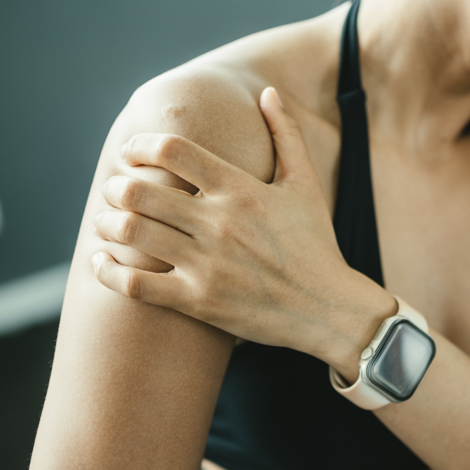 Female athlete holding painful shoulder in gym, representing shoulder pain, rotator cuff injury, sports injury and physical therapy rehabilitation concept.