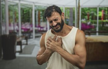Man clutching chest with both hands on a covered restaurant patio inside a building, grimacing; pain.