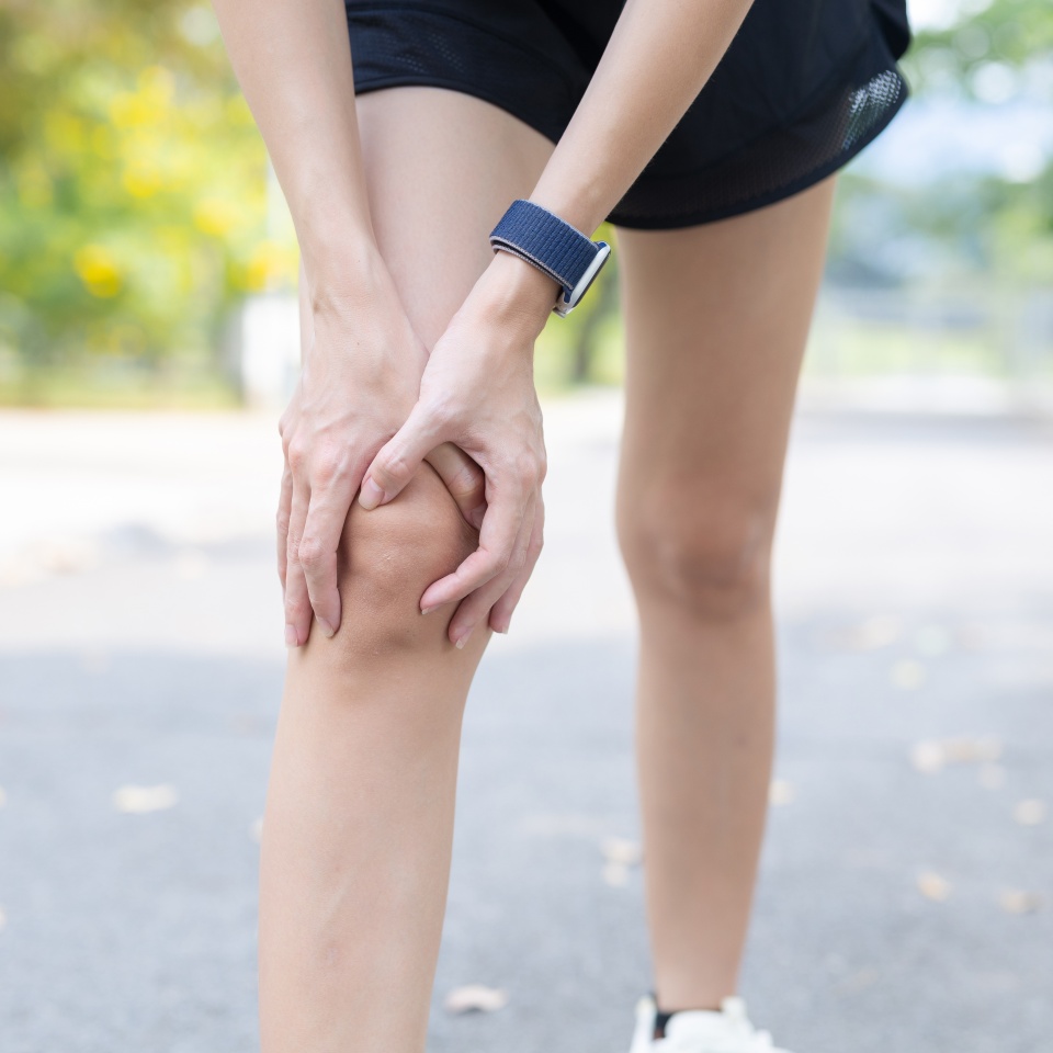 Female runner holding her knee experiencing severe pain and physical discomfort after an outdoor injury stopping on road touching hurting leg joint showing suffering during an exercise routine