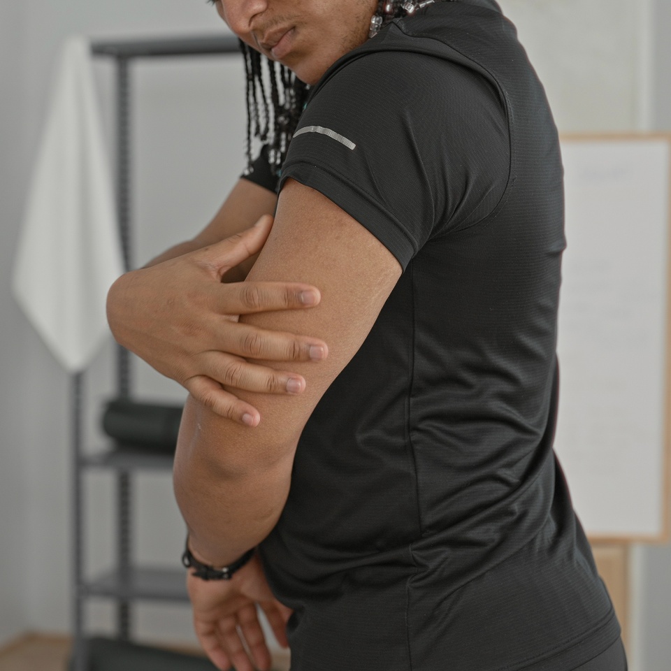 Man holds upper arm and massages it for muscle strain after workout in fitness studio; recovery discomfort resilience.