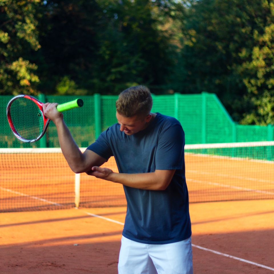 Handsome man on tennis court. Young tennis player. Pain in the elbow