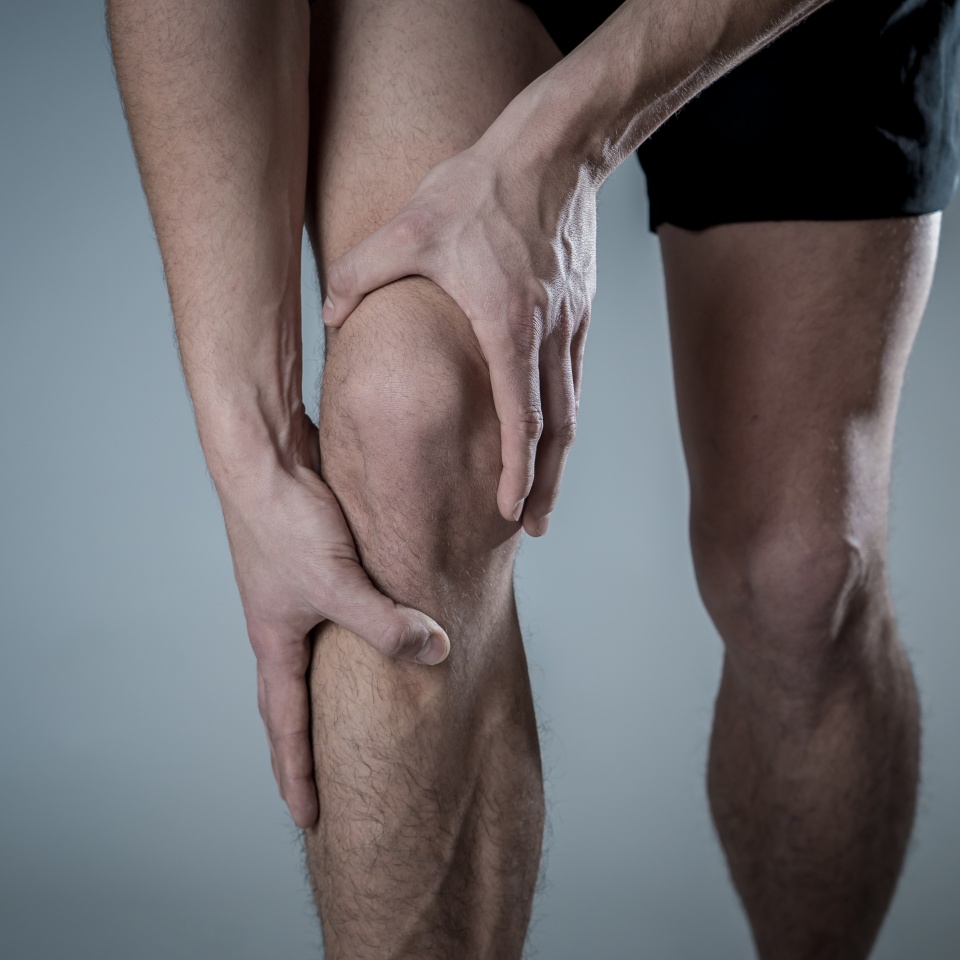 Young fit man holding knee with hands in pain after suffering muscle injury broken bone leg pain sprain or cramp during running workout. In Body pain and sport training injury and body health care.