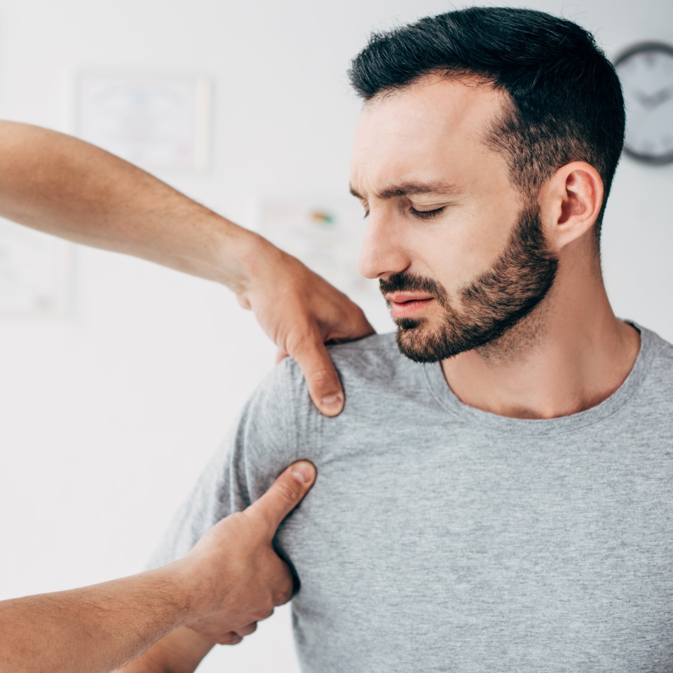 Selective focus of patient sitting on couch and doctor massaging patient shoulder in massage cabinet at clinic