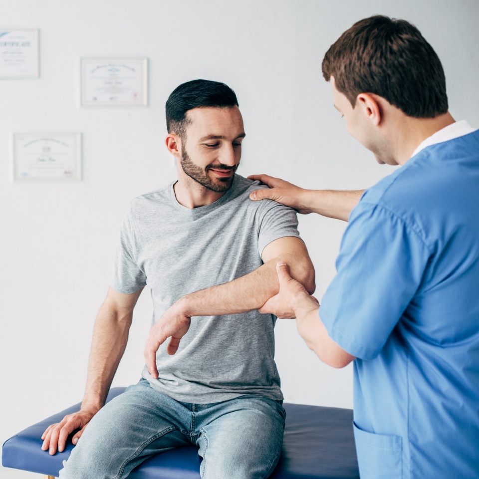 Selective focus of chiropractor examining patient shoulder in massage cabinet at clinic