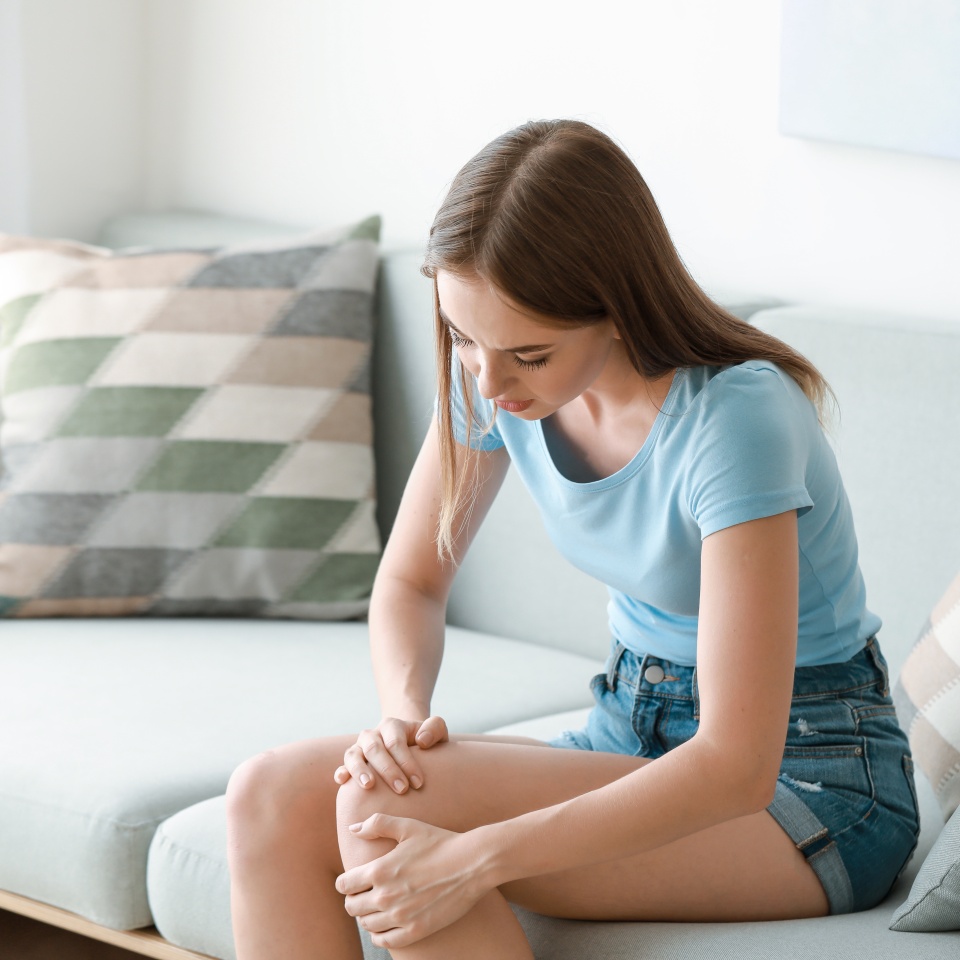 Young woman suffering from pain in knee at home