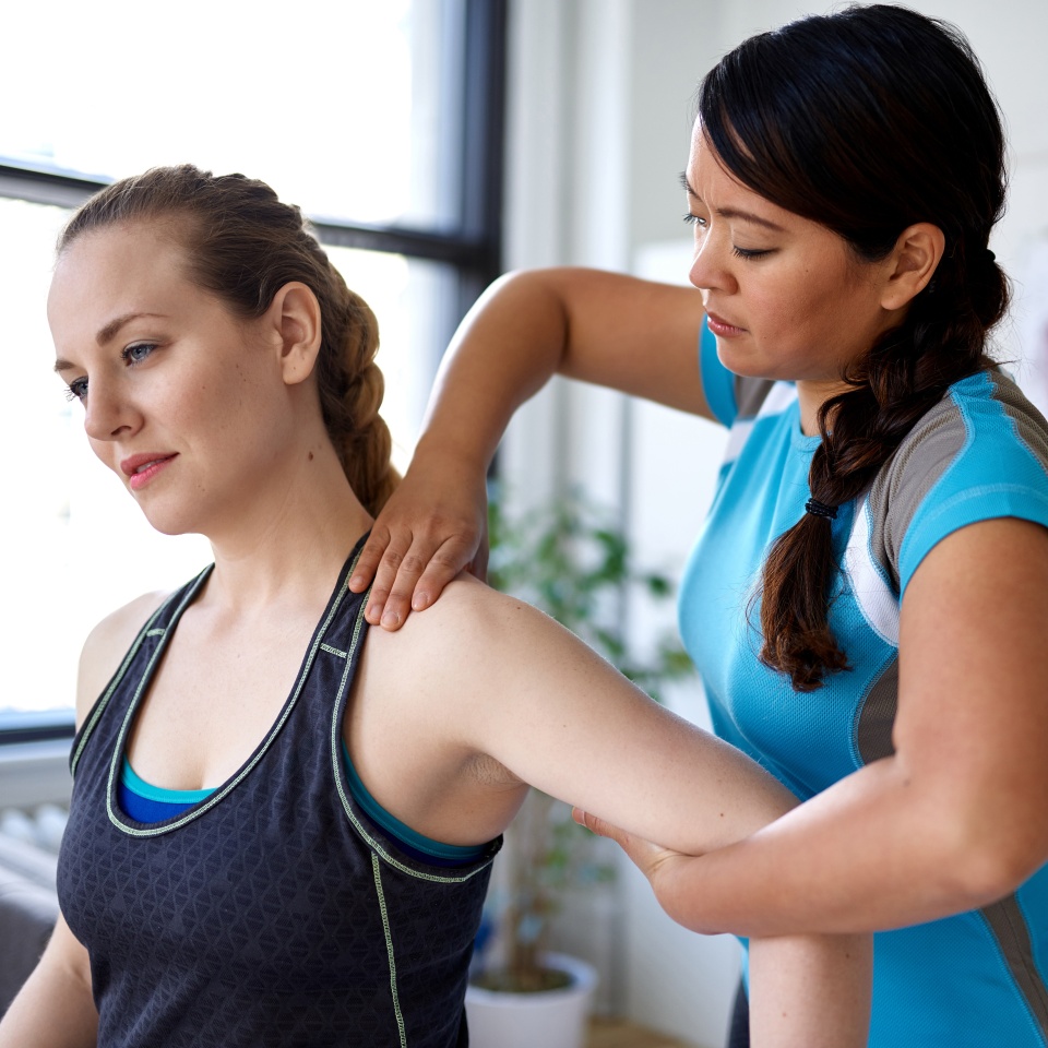 Candid image of an attractive patient during a appointment with professional asian physiotherapist in design kinesio clinic working and massaging her neck and shoulder pain