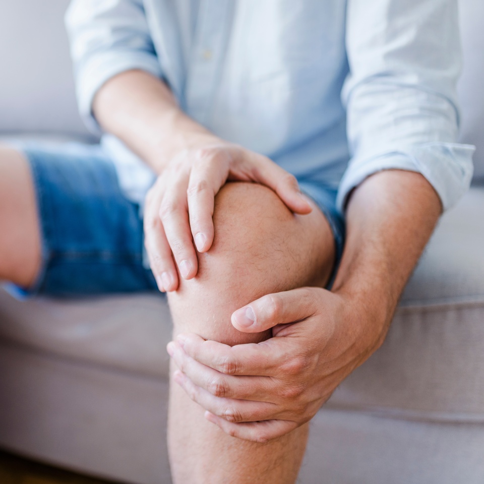 Man suffering from knee pain sitting sofa. A mature man massaging his painful knee. Man suffering from knee pain at home, closeup. Pain knee