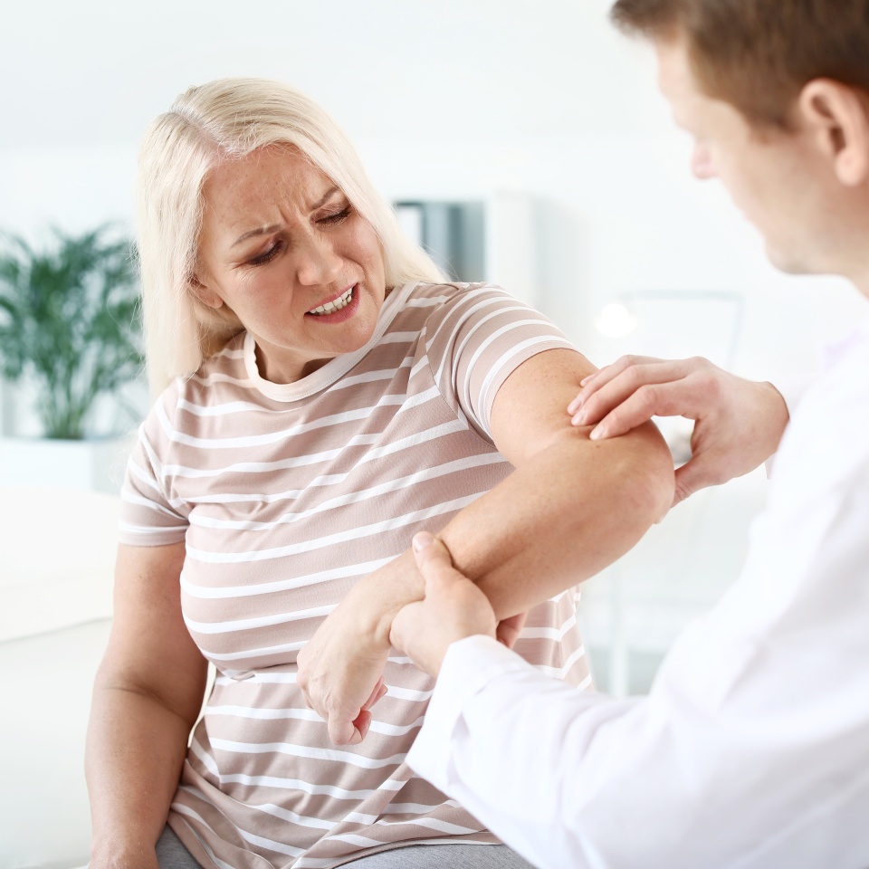 Doctor examining mature woman with joint pain in clinic