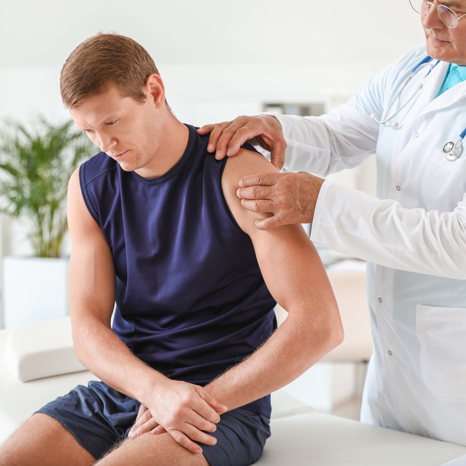 Mature doctor examining sportsman with joint pain in clinic