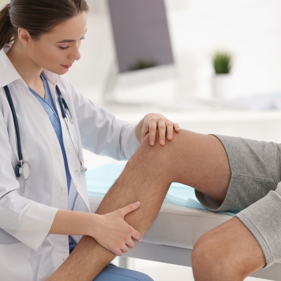 Female orthopedist examining patient's leg in clinic, closeup
