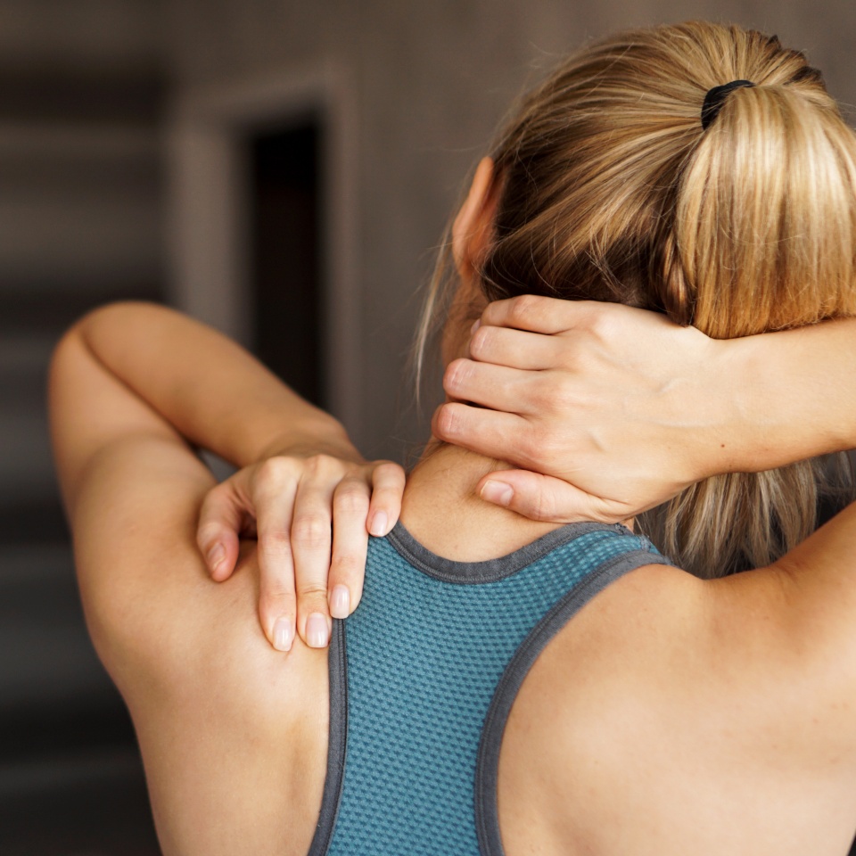 Sports injury concept. Athletic girl feeling pain in her neck against blurred background. Pain after home workout