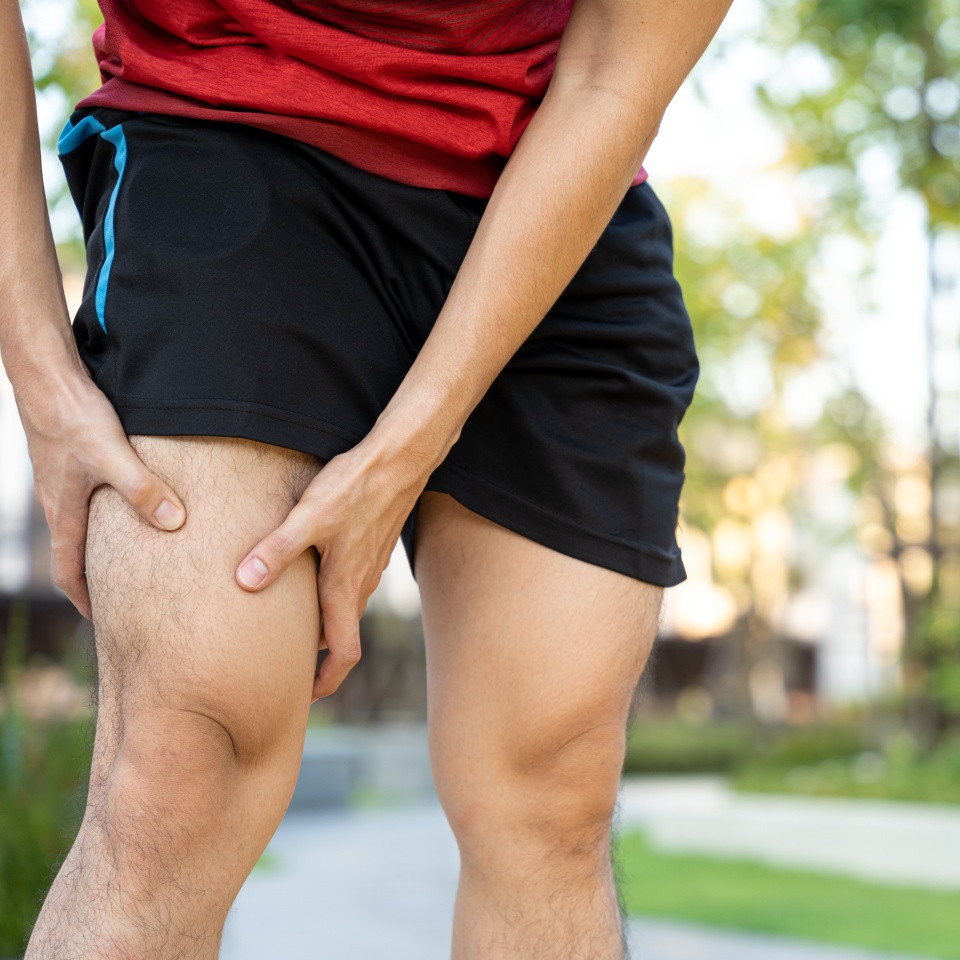 Male runner athlete leg injury and pain. Hands grab painful knee while running in the park.
