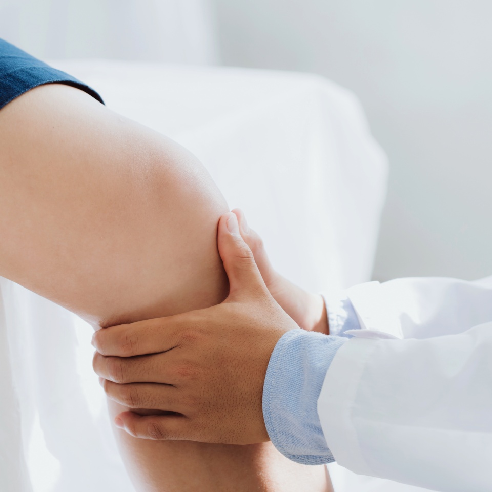 Doctor physiotherapist working examining treating injured knee of patient, his using the handle to the patient knee to check for pain.