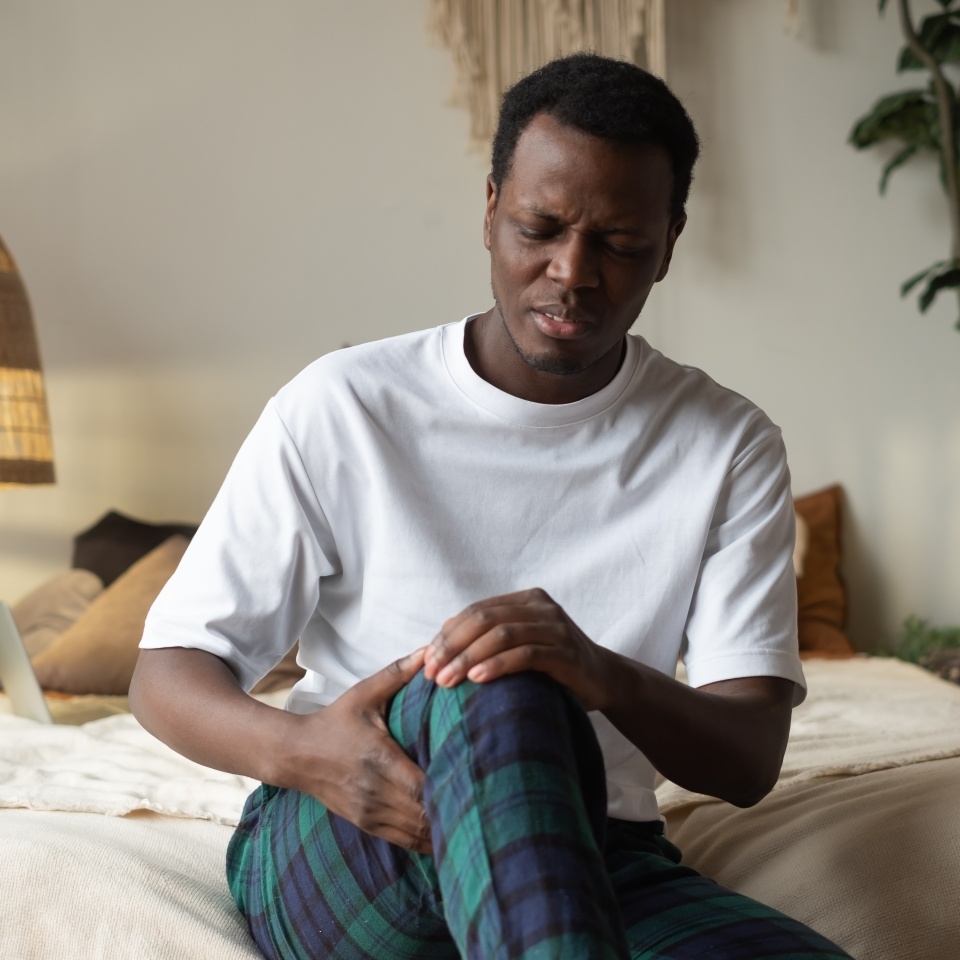African man suffering from knee pain sitting sofa. A mature man massaging his painful knee.