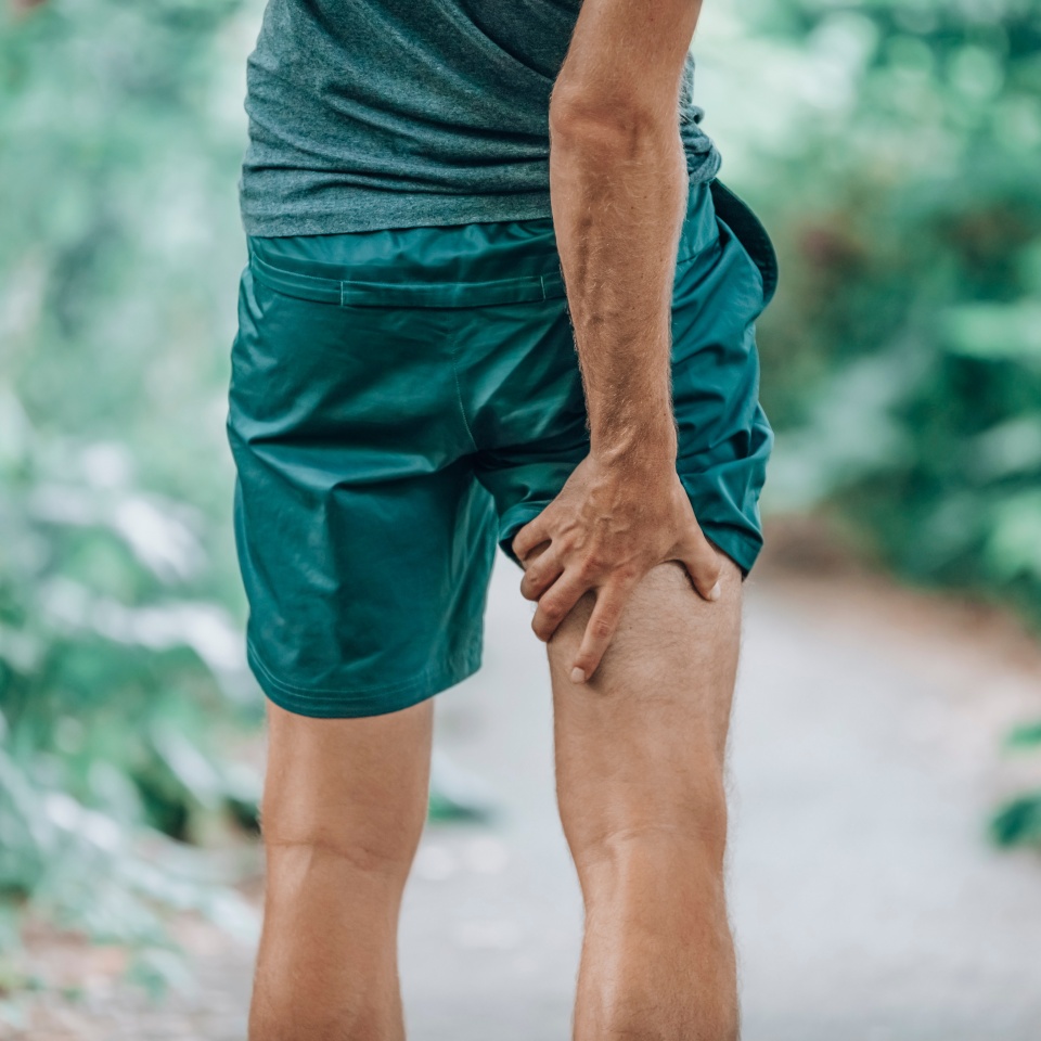 Leg muscle pain sports injury runner man touching painful hamstring muscle. Legs physiotherapy care athlete massaging sore muscles during running training in summer park outside.