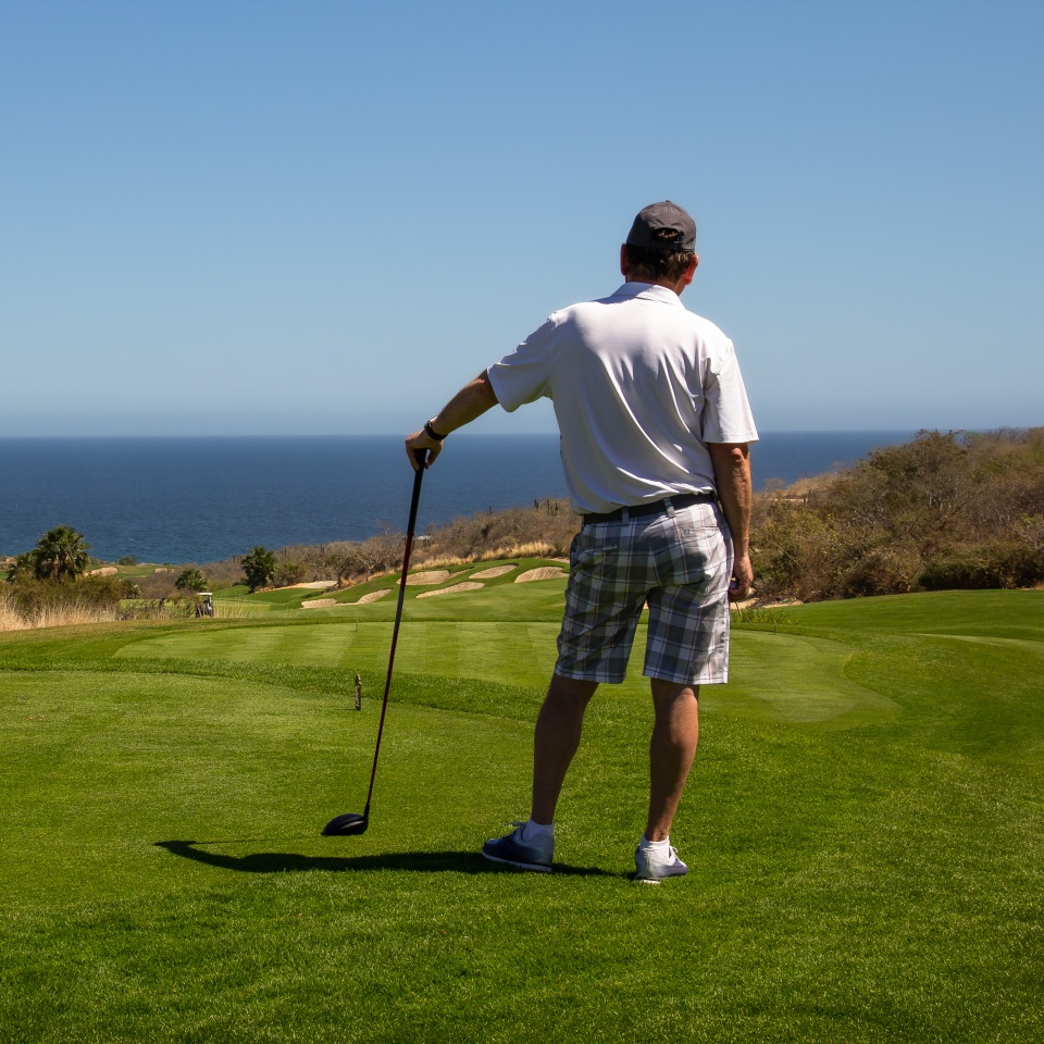 Middle aged man looking out over ocean side tropical golf course view while waiting to tee off. Copy space.