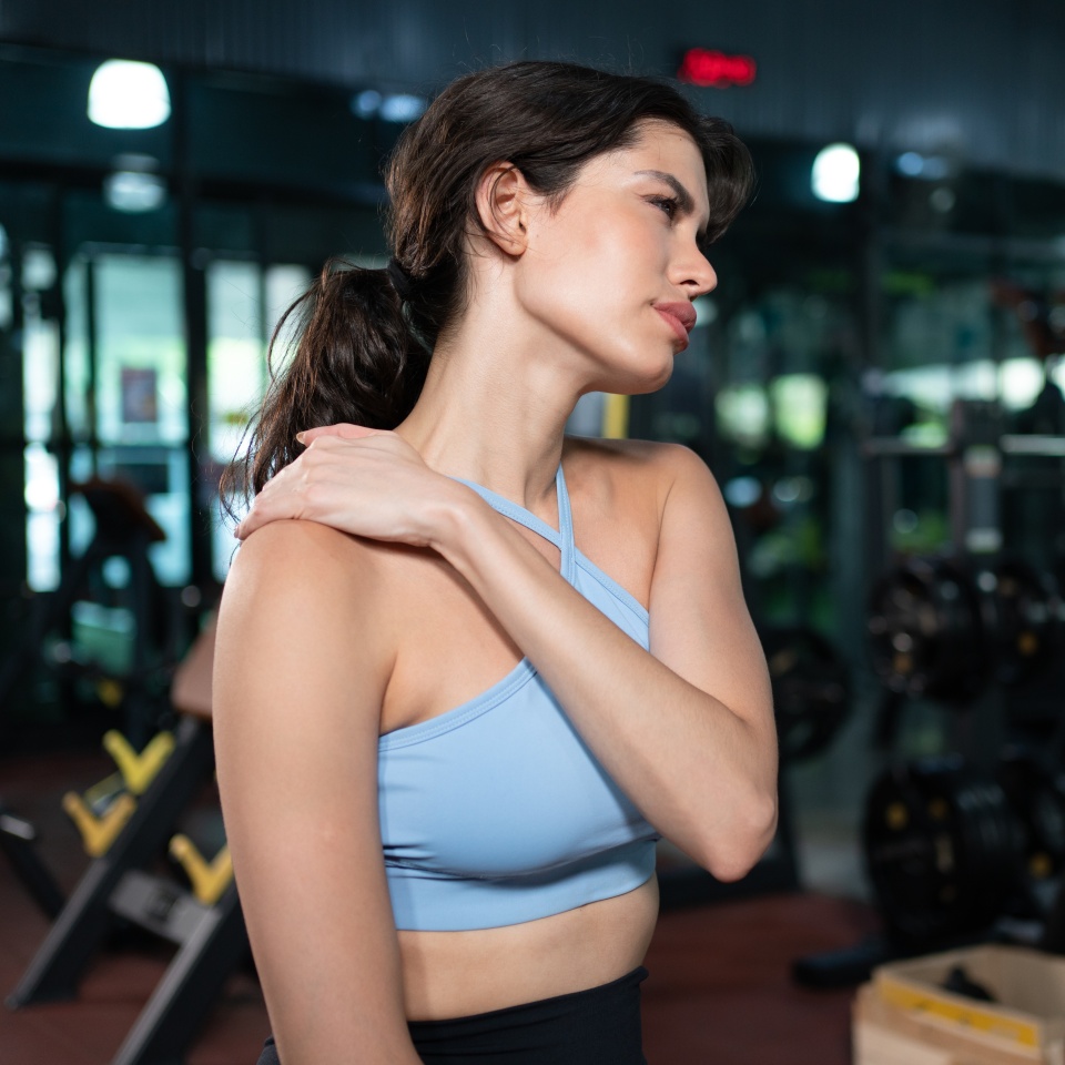 Young woman feeling pain in her shoulder muscle after fitness workout at gym