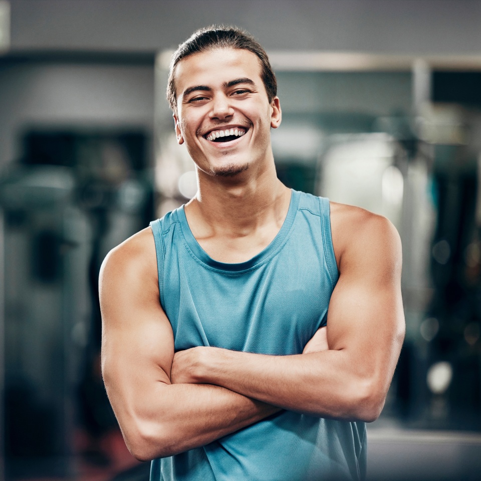 Fitness, gym and happy portrait of personal trainer man ready for workout coaching. Training, wellness and exercise coach confident with arms crossed at professional athlete health club
