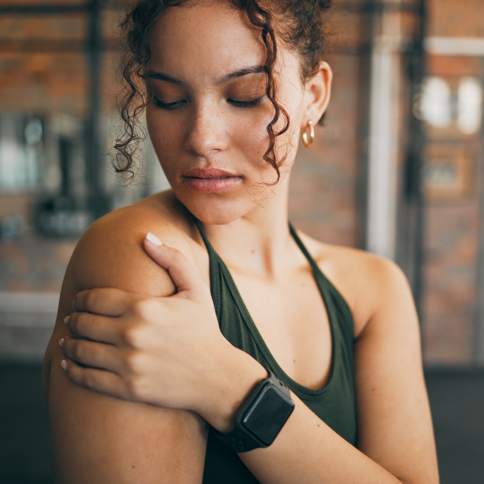Woman, shoulder pain and muscle injury from sports workout, exercise or training at the gym indoors. Female holding arm after painful sport accident, inflammation or bruise from intense exercising.