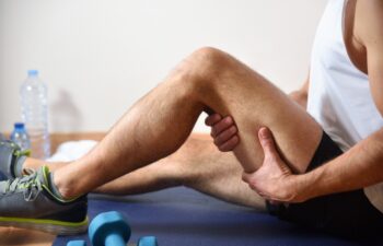 Detail of man doing sports with hamstrings pain holding himself with his hand sitting on a mat. Side view