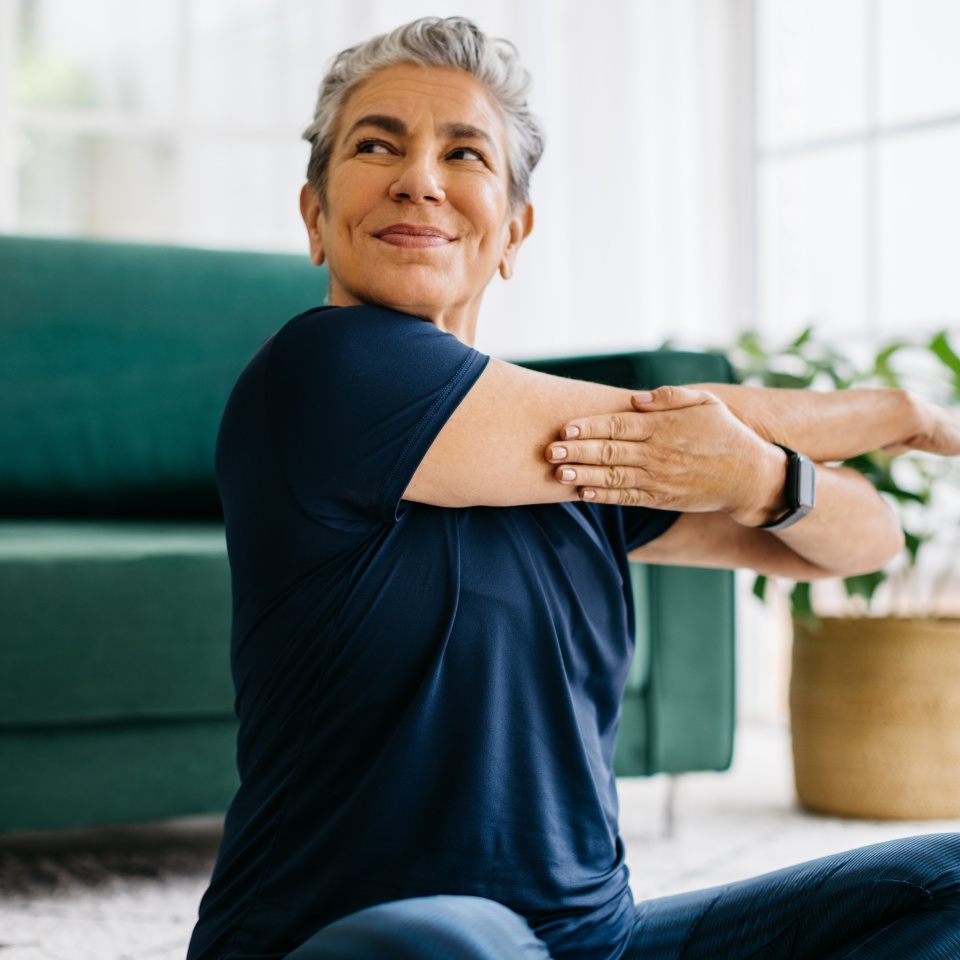 Happy and healthy senior woman doing a shoulder mobility exercise at home, working out with a cross arm stretch in her yoga session. This mature woman is keeping herself active with a fitness routine, maintaining physical wellbeing and wellness as she ages.