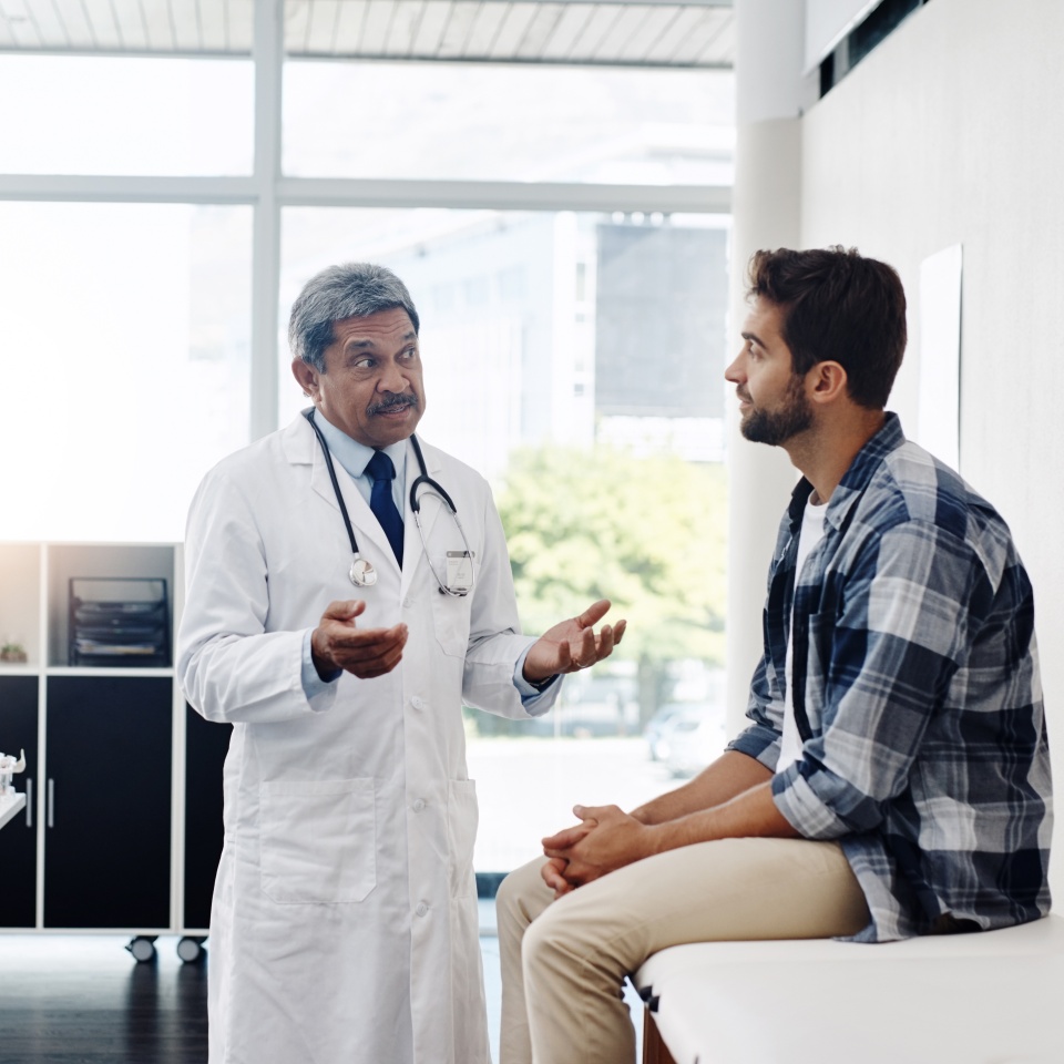Healthcare, doctor and patient in consultation with expert advice, information and support in discussion. Medicine, health care and Indian man in doctors office consulting with medical professional