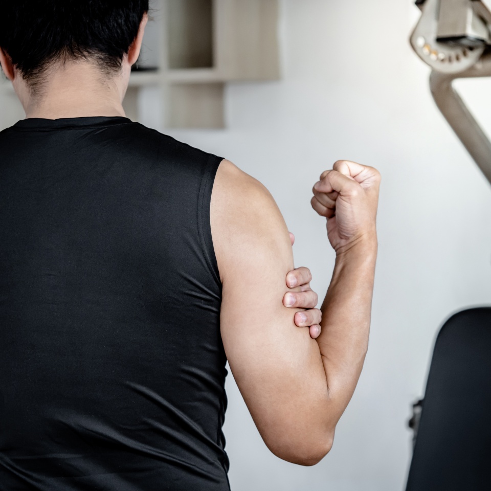 Sportive man feeling upper arm muscle pain after doing weight training exercise in fitness gym. Male athlete suffering from acute bicep muscular inflammation symptom. Sport injury concept