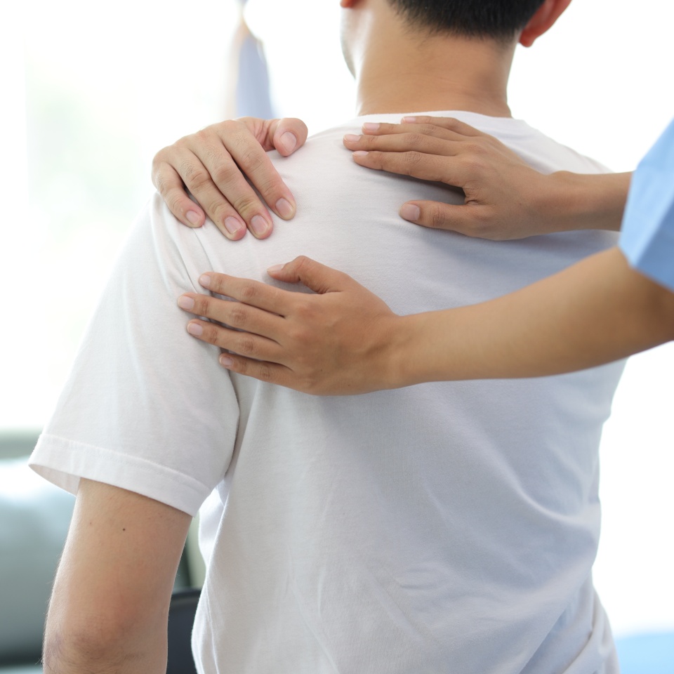 Doctor diagnosing man's shoulder pain in hospital examination room. Nurse doing massage and physiotherapy to treat patient's shoulder.