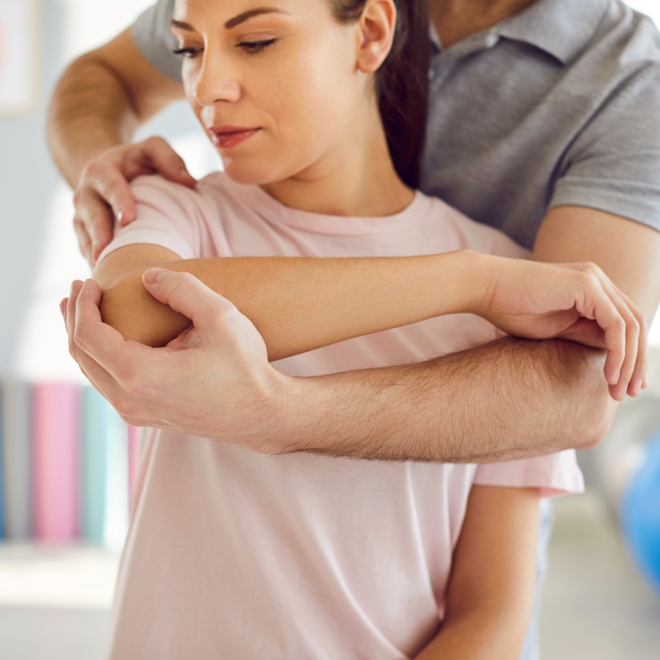 Woman getting treatment at clinic of chiropractic, physiotherapy or osteopathy. Physiotherapist, chiropractor or osteopath helps female patient do medical exercise for her arms and shoulders correctly
