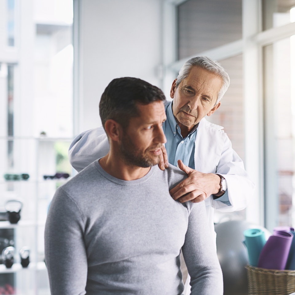 Doctor, man and patient in consultation for shoulder pain with physical therapy, healthcare or body recovery. Orthopedic, physician or medical expert for arm rehabilitation with examination or advice.