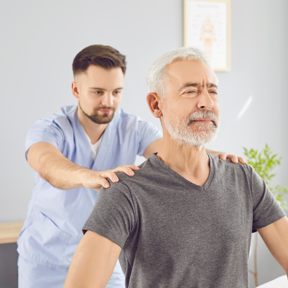 A rehabilitation doctor straightens the shoulders of an elderly man, close-up. Professional medical intervention in a rehabilitation center. Concept medical services, physiotherapy