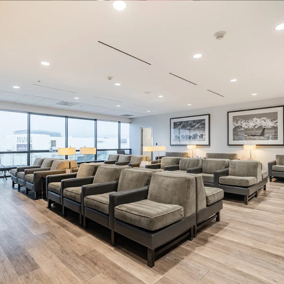 Modern medical office waiting room with rows of gray upholstered chairs, wood flooring, black and white nature photography on walls, and large windows overlooking the Beverly Center.