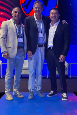 Dr. Reza Jazayeri, M.D. posing with two men on stage at a conference event with blue lighting backdrop.