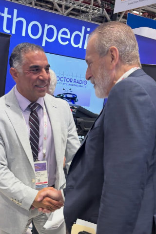 Dr. Reza Jazayeri, M.D. shaking hands with a man at an orthopedic industry event or trade show booth.