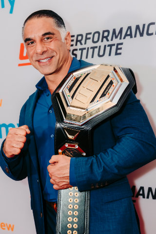 Dr. Reza Jazayeri, M.D. smiling and posing with a championship belt at a Performance Institute event.