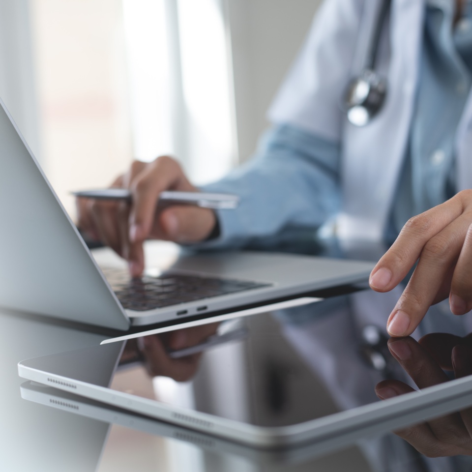 Doctor using digital tablet and working on laptop computer at doctor's office in hospital, close up. Healthcare and medicine, medical technology background