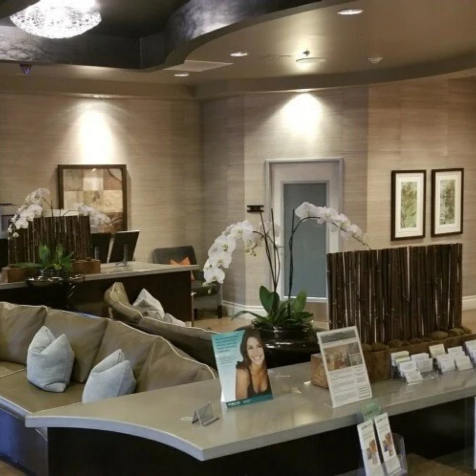 Elegant spa or medical office reception area with tan sofa, bamboo decor, white orchids, and product displays on curved counter.