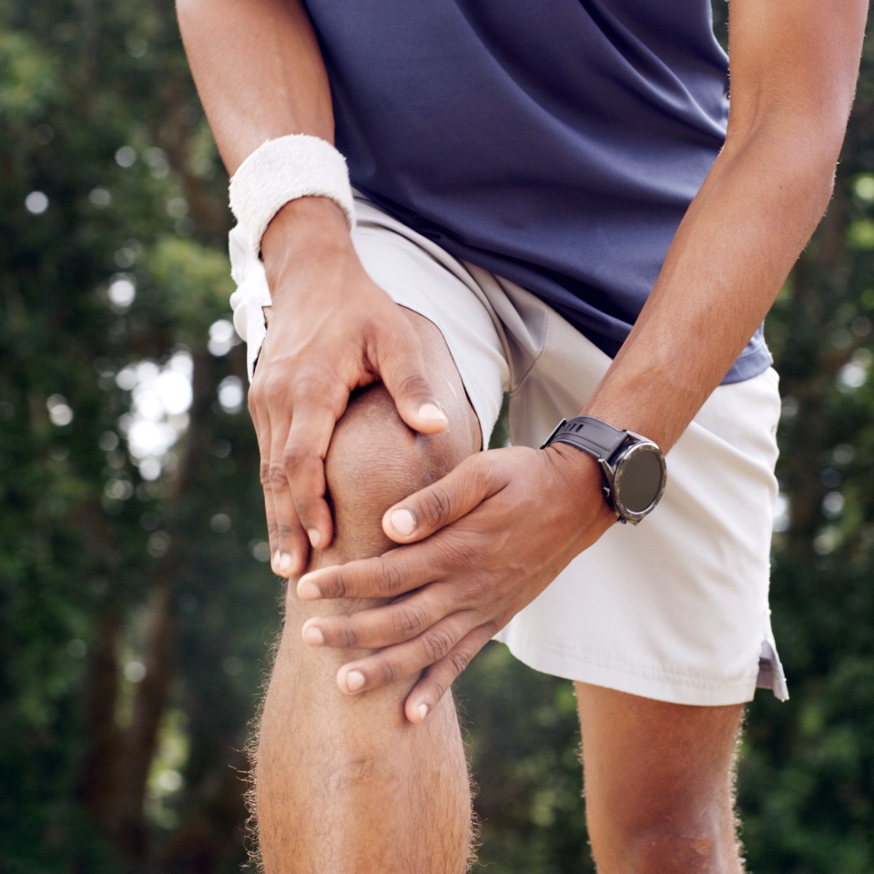 Fitness, hands and man with knee pain outdoor from sports injury, muscle fatigue and workout strain. PFPS, runner and kneecap dislocation in nature with joint inflammation, exercise sprain and bokeh.